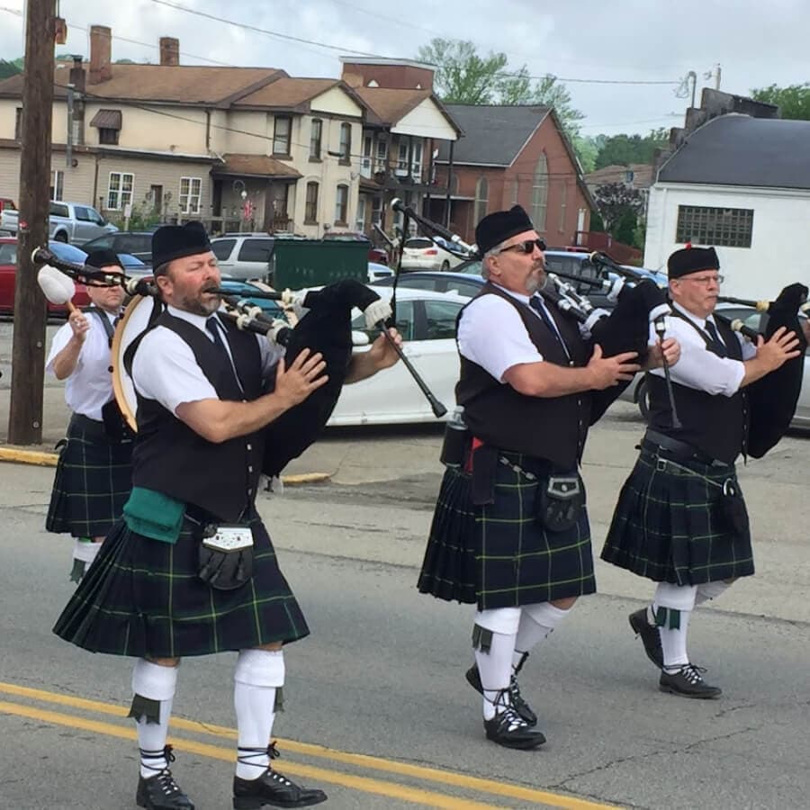 Three men in kilts play bagpipes during a parade.